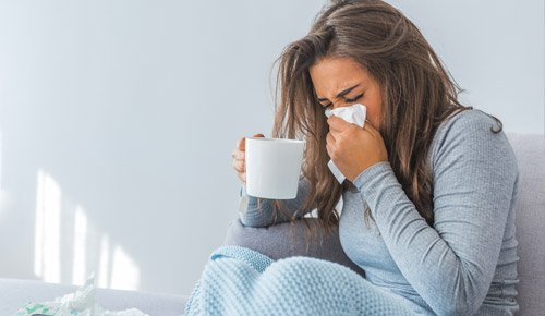Woman sneezing into tissue and holding coffee