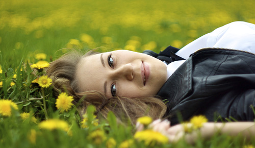 Woman smiling and laying on the grass next to flowers