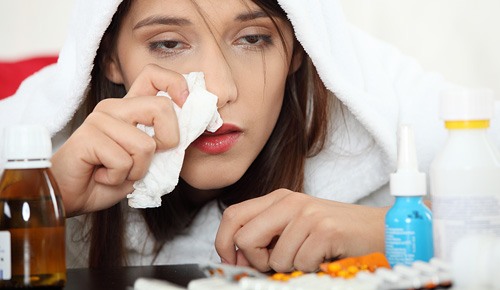 Woman sick in bed with a bunch of tissues and medicine