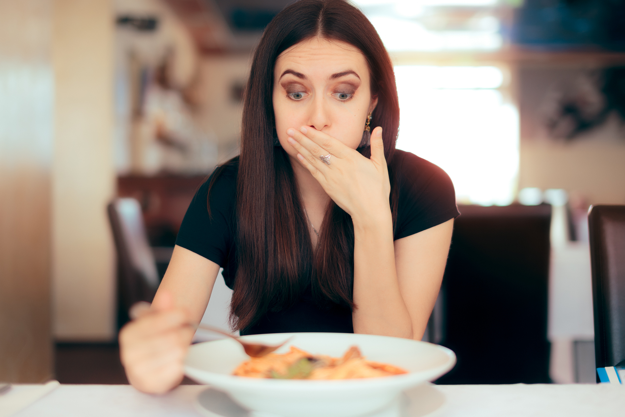 Woman eating pasta holding mouth in shock